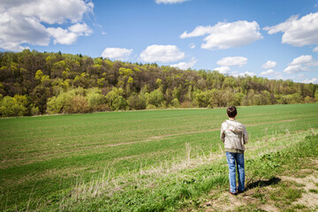 Fototapeta na wymiar The boy stands in front of the field and the forest. Sunny summer day.