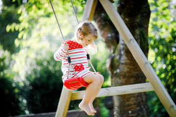 Happy beautiful little toddler girl having fun on swing in domestic garden. Cute healthy child...