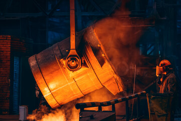 Molten metal in big ladle container and unrecognizable worker. Iron casting in metallurgy foundry...