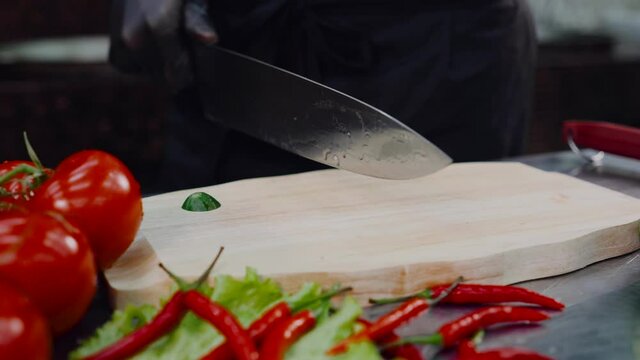 Knife sheff cuts the cucumber. Slicing vegetables on wooden cutting board.