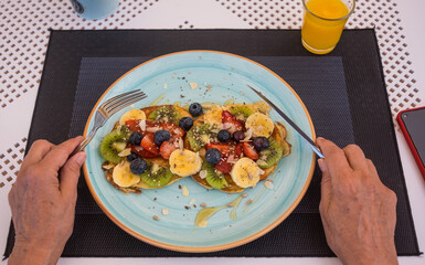 Woman's hands on table with classic american pancakes for breakfast, fresh fruit and honey. Healthy eating concept