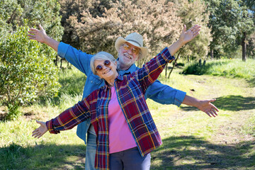 Playful senior couple walking in the forest with arms outstretched. Two happy retired enjoying...