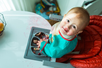 Portrait of a baby of 8 monthes eating with hands from plate with sections, shot from the top view.