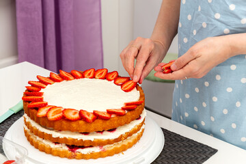 The woman decorates the cake with strawberries.
