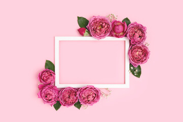 Flower border frame made of rose on a pink pastel background. Greeting card template with copyspace. Nature composition.