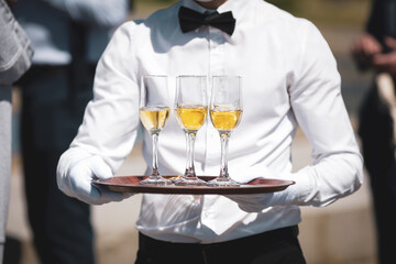 Shallow depth of field (selective focus) details with a waiter walking around and giving sparkling wine to the guests of an event.