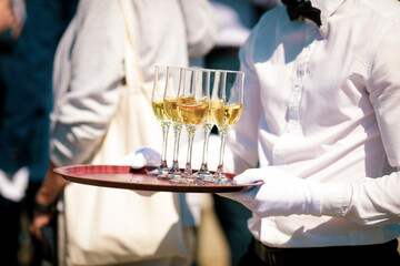 Shallow depth of field (selective focus) details with a waiter walking around and giving sparkling wine to the guests of an event.