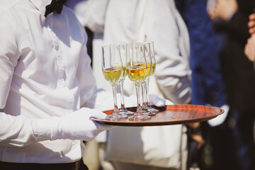 Shallow depth of field (selective focus) details with a waiter walking around and giving sparkling wine to the guests of an event.