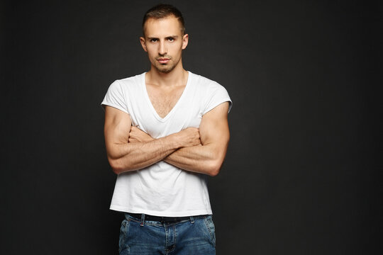 A confident young guy in a white blank t-shirt and jeans posing over black background. A handsome adult man in a casual outfit posing in the dark background with crossed arms