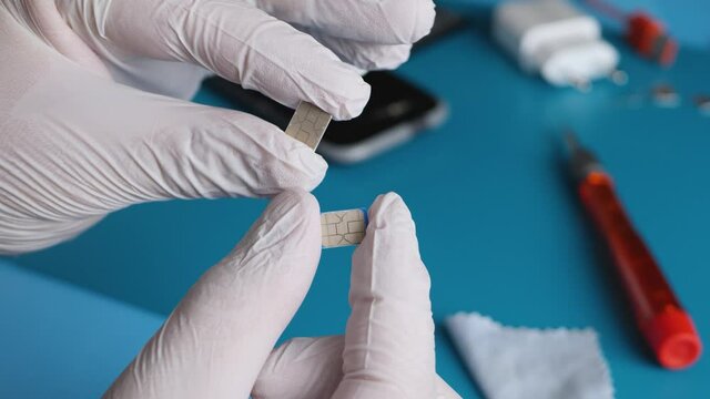 Equipment engineer's hand in white gloves hold nano-SIM cards. Mobile phone background disassembled. Communication repairman. Service for repair of mobile device. 5g network and technology concept