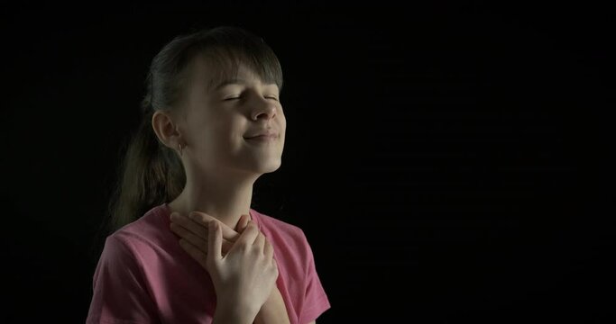 The girl is praying. Teenage girl in prayer on a black background.