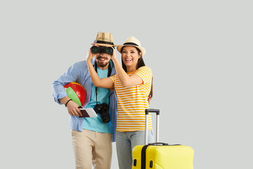 Happy smiling couple in love with suitcase and beach accessory standing over studio grey background. Overjoyed woman wife holding binocular helping man husband looking through. Tour searching