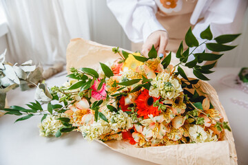 a female florist in a white shirt wraps a bouquet of fresh assorted colorful flowers in craft paper.