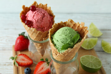 Cones with ice cream and ingredients on white wooden background