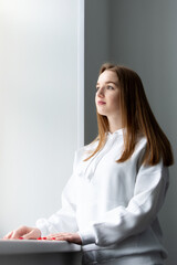 young woman with long hair stands at the window.