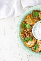 Fried slices of zucchini with sour cream sauce on plate. Fried courgettes with herb for dinner on white background