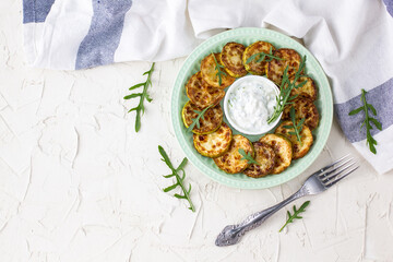 Fried slices of zucchini with sour cream sauce on plate. Fried courgettes with herb for dinner on white background