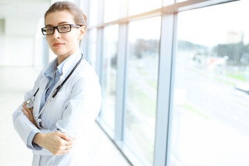 Beautiful woman doctor with stethoscope smiling charmingly and ready to help patients in sunny hospital. Medicine concept