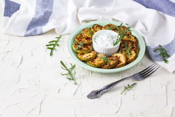 Fried slices of zucchini with sour cream sauce on plate. Fried courgettes with herb for dinner on white background