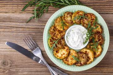 Fried slices of zucchini with sour cream sauce. Courgettes with herb for dinner on natural wooden background