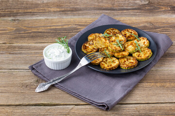 Fried slices of zucchini with sour cream sauce. Courgettes with herb for dinner on natural wooden background