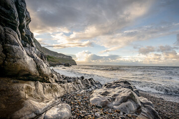 Beautiful golden hour sunset of ocean rocky cover and pebble beach on North Wales coastline. ...