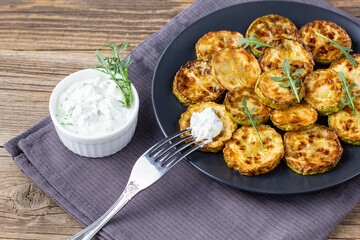 Fried slices of zucchini with sour cream sauce. Courgettes with herb for dinner on natural wooden background