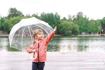 happy little girl with umbrella in the rain by the pond