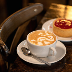 Cappuccino coffee with berry dessert on dark background. Sweets and Cup of creamy drink with froth. Square format, soft focus. Close up shot. Copy space.