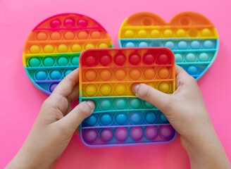 colorful antistress sensory toy fidget push pop it in kid's hands on pink background