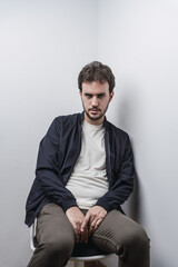 Vertical shot of a Caucasian man with an intense stare while seated on a chair at a corner of a room