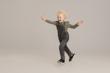 Happy Caucasian little albino boy running isolated over gray studio background.