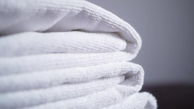 Concept of hygiene and cleanliness. Household, hotel,hostel, spa. Close up of hands putting stack of fresh white bath towels on the bed.