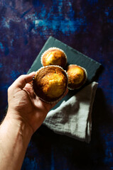 Hand picking up a muffin from the slate plate with linen cloth on a rusty blue background. Dark food. Selective focus