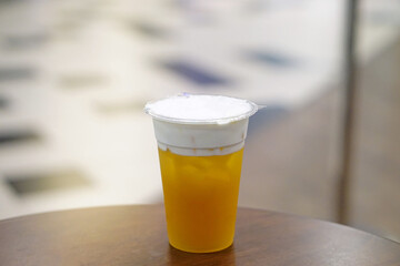 Hand holding plastic glass of iced oolong tea (also called wulong or wu long) with layer of cream cheese foam on blurred background.