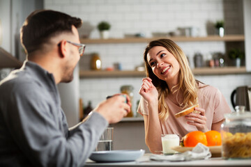 Beautiful young girl enjoying in breakfast with her boyfriend. Loving couple drinking coffee in the kitchen
