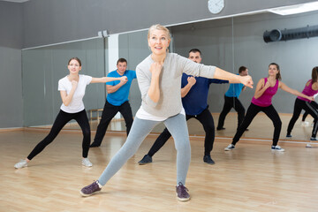 Fototapeta na wymiar Smiling mature female doing dance workout during group classe in fitness center