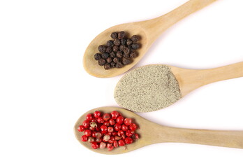 Red and black peppercorns and ground white pepper pile in wooden spoons isolated on white...