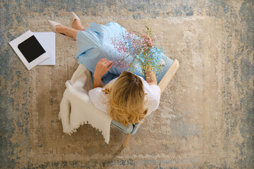 View from above at a woman sitting in armchair with flowers in hand