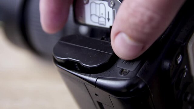 A photographer changes the battery in his SLR camera. Focus on the camera battery
