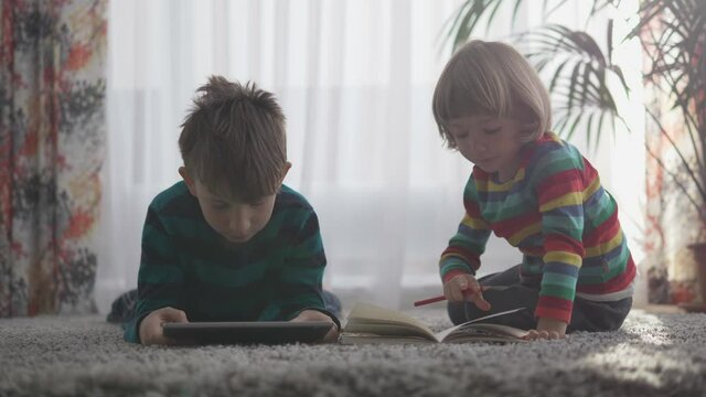 Brothers doing their homework, big boy with tablet, little child with pencil and notebook
