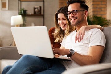 Happy young couple with laptop at home. Boyfriend and girlfriend watching movie on laptop