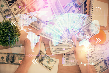 Double exposure of world map drawing hologram and us dollars bills and man hands.