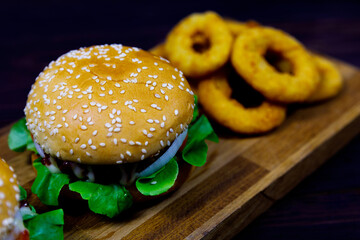 Closeup top view shot of two delicious tasty yummy hamburgers bun with beef tomato and lettuce serve with fried onion rings on wood plate decorated on sack cloth with parsley on dark old wooden table