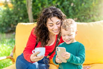 happy mom and son chilling outdoor sitting on couch in public park garden watching funny videos on smartphone. smiling woman and child interacting online on apps. tech, social media influencer concept