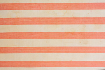 A fragment of the upholstery of an old mattress with red and white stripes. The fabric is aged, there are traces of dirt and liquid drips. Background. Texture.