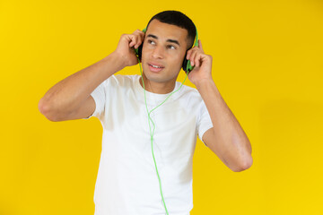 Young handsome man wearing headphones listening music isolated over yellow background.