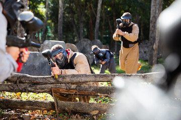 Men and women in protective uniform playing paintball on shooting range