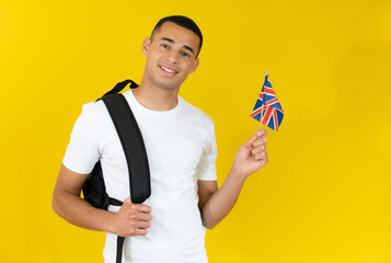 Happy handsome student holding a british flag isolated over yellow background