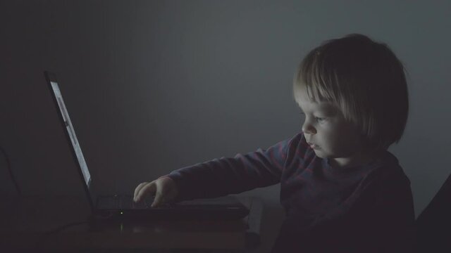 Portrait of little baby child at computer in dark night, burning work, dream time